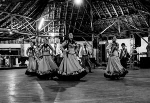Eventos Black and white image of a cultural dance performance in a rustic indoor setting.