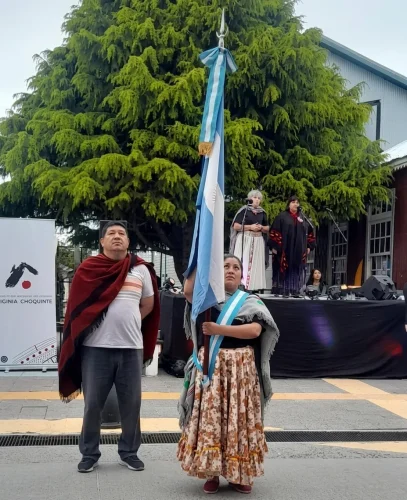 Integrantes con trajes folclóricos tradicionales portando la Bandera Argentina en un acto al aire libre